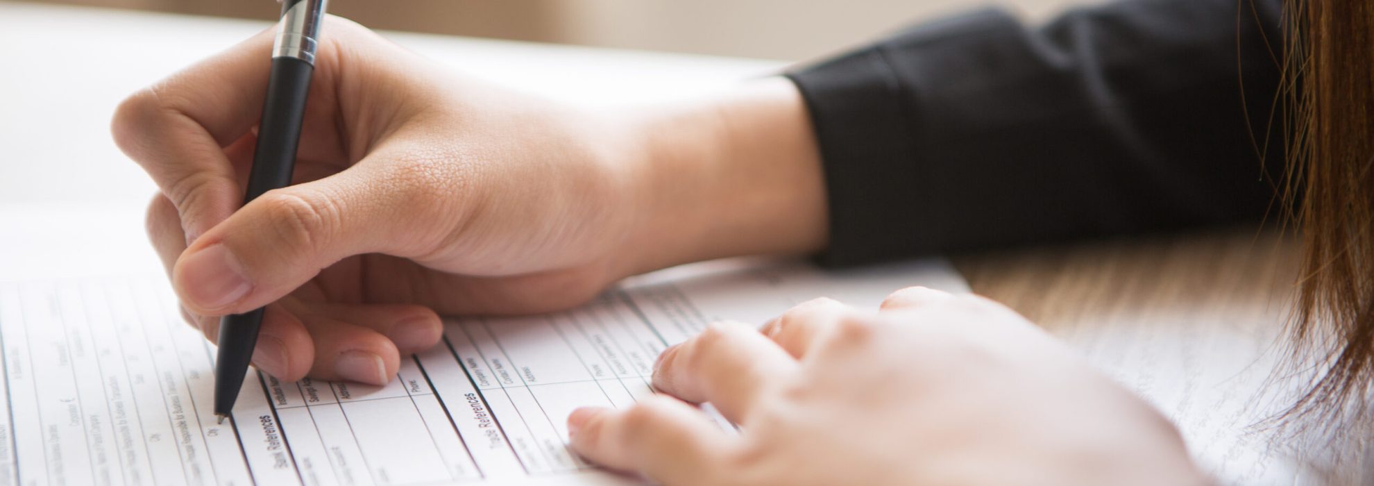 Cropped View of Woman Filling in Application Form Cropped view of woman holding pen and filling in application form at table